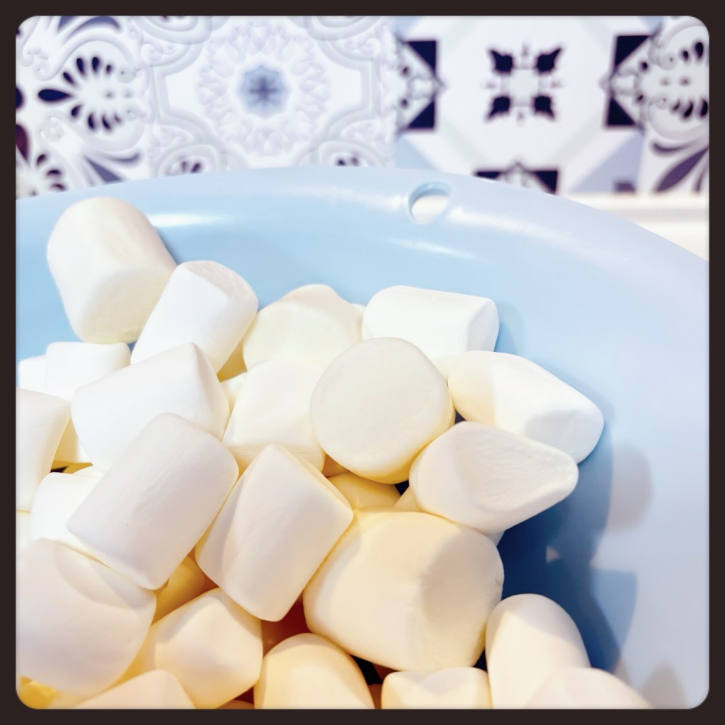 A light blue bowl, filled with medium-sized, fluffy, white marshmallows.