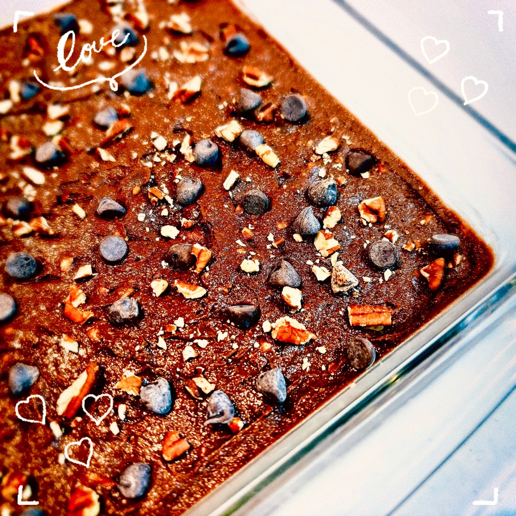 A corner of a glass pan, filled with brownie batter, and sprinkled with chocolate chips and chopped pecans.