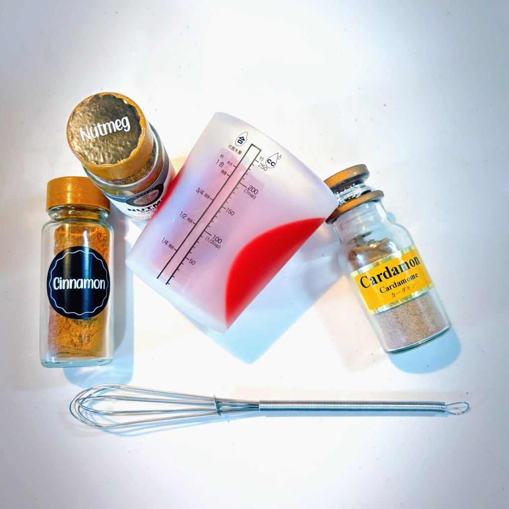 Jars of cinnamon, nutmeg, and cardamom, as well as a small, flexible, silicone measuring cup and a mini whisk.