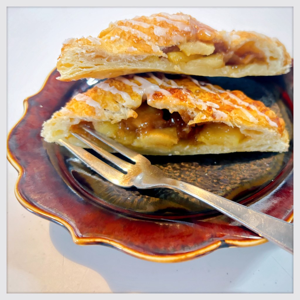 A small, square apple pie, sliced into two triangles to show off its apple-y interior.