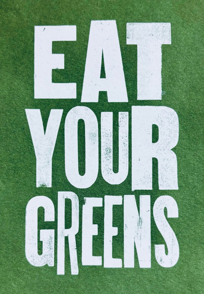 A postcard which has an irregularly sized, all caps font, and states, "EAT YOUR GREENS".