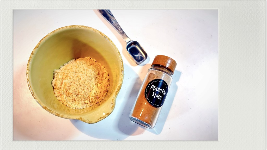 A small, yellow ceramic bowl with brown sugar in it, next to a bottle of apple pie spice.