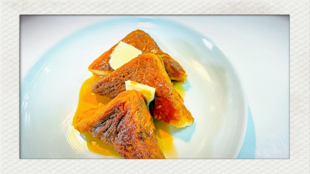 A plate with three triangular slices of Canadian French Toast on it, as well as a couple pats of butter, and a small pool of maple syrup.