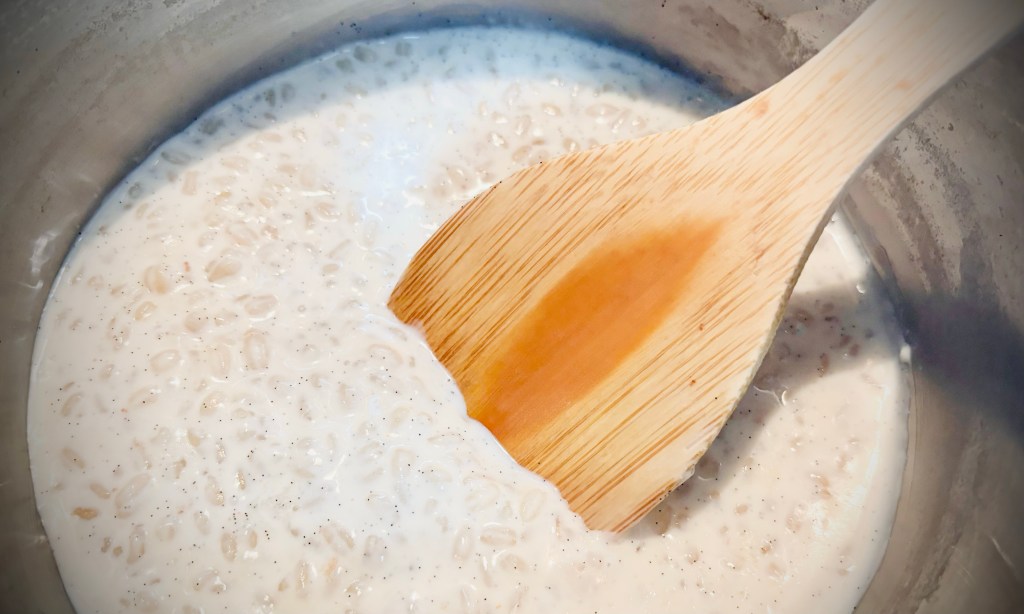 An overhead view of rice pudding and a wooden spoon in a metal pot.