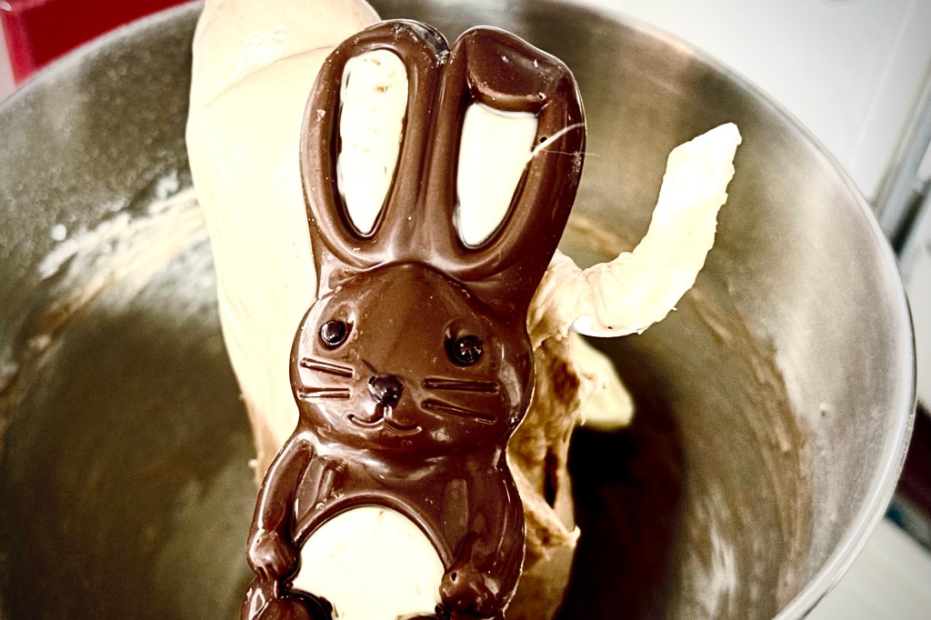A chocolate Easter bunny sits in the precipice of a stand mixer, ready to join its brethren with the dough and the bread hook inside of the bowl. Bye bye!