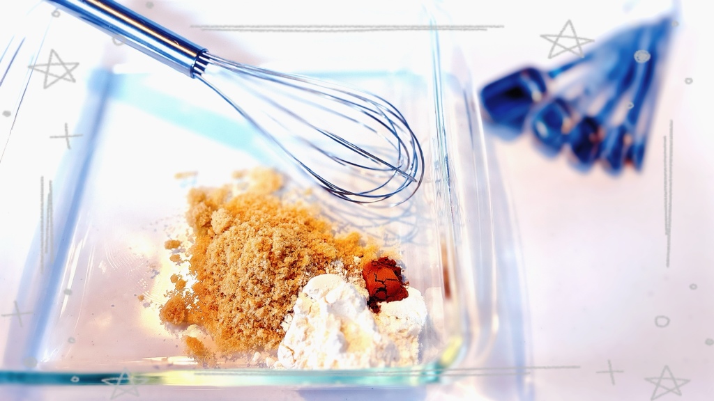 A square glass pan with dry ingredients such as flour, sugar, and cinnamon piled in one corner. There is also a whisk in the pan, and a glass of peach syrup in the background.