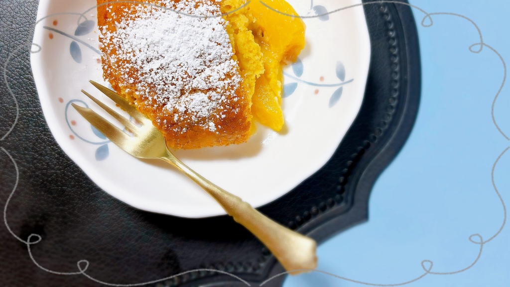 A square slice of peach cobbler in a bowl. It is golden brown on top, and yellow-orange peaches peeking out of the bottom. It is dusted with powdered sugar, and there is a golden dessert fork in the bowl.