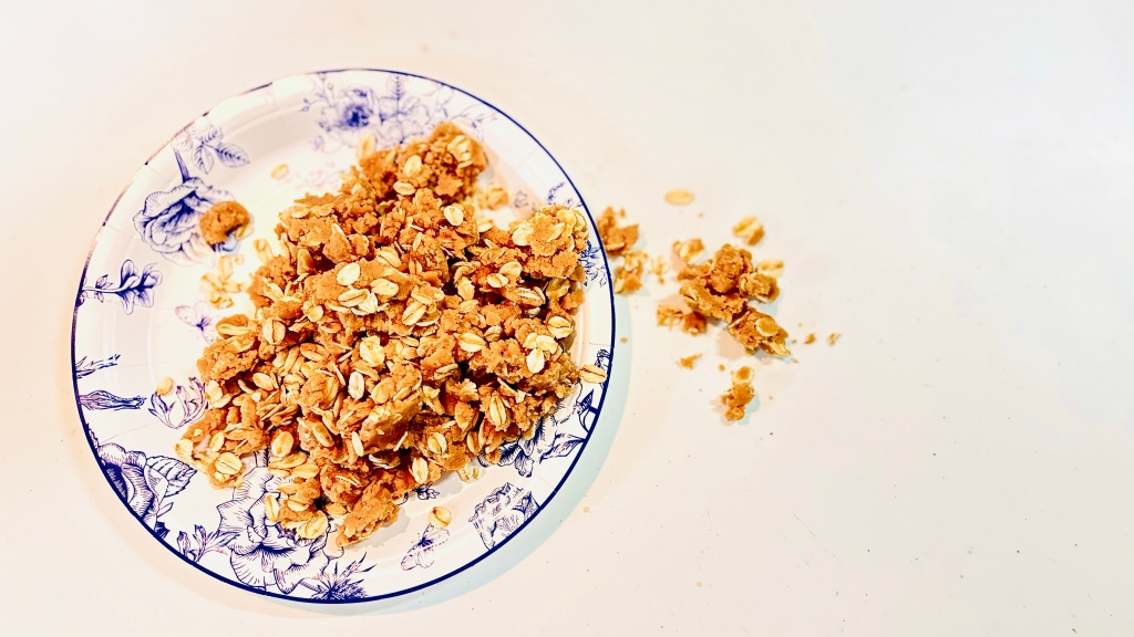 A big pile of oatmeal streusel falling off the side of a small white and blue plate.